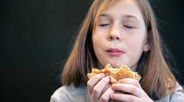 Una bambina con le lentiggini mangia un hamburger