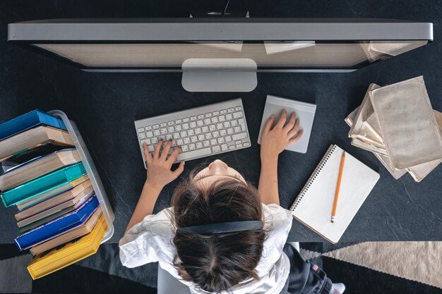 Una bambina con libri e quaderni si siede davanti alla vista dall'alto del computer