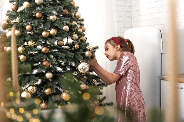 Una bambina decora un albero di natale appende le palle