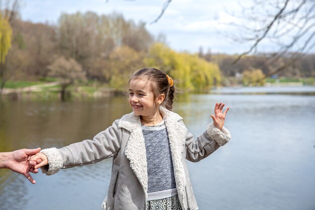 Una bambina in una passeggiata nel parco all'inizio della primavera tiene la mano di suo padre.