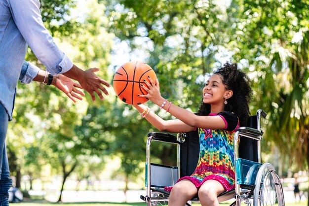 Una bambina su una sedia a rotelle si diverte con suo padre mentre giocano a basket insieme al parco