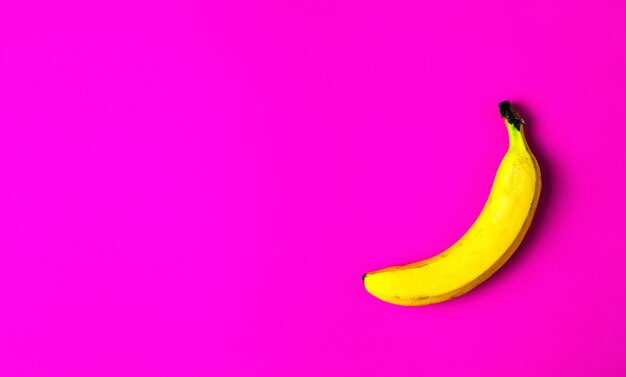 Una banana gialla matura su una superficie rosa brillante