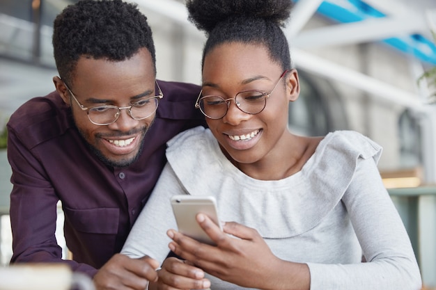 Una bella coppia africana naviga in Internet su uno smartphone, prenota i biglietti online mentre trascorre le vacanze estive in un paese tropicale, ha espressioni felici.