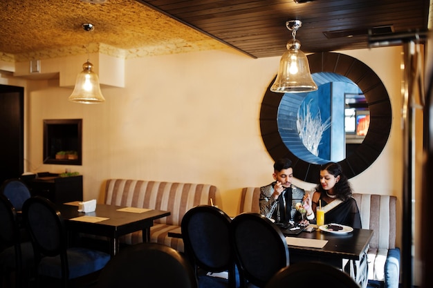 Una bella coppia indiana innamorata indossa un abito elegante e saree seduto al ristorante e mangiando il gelato insieme