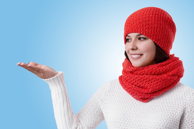 Una bella donna con un sorriso piacevole che indossa abiti invernali caldi in piedi lateralmente alzando la mano e guardando da parte