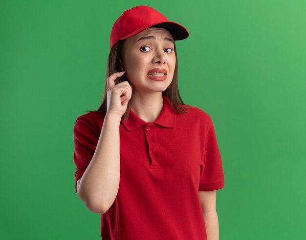 Una bella donna delle consegne ansiosa in uniforme tiene la mano vicino al viso e guarda di lato