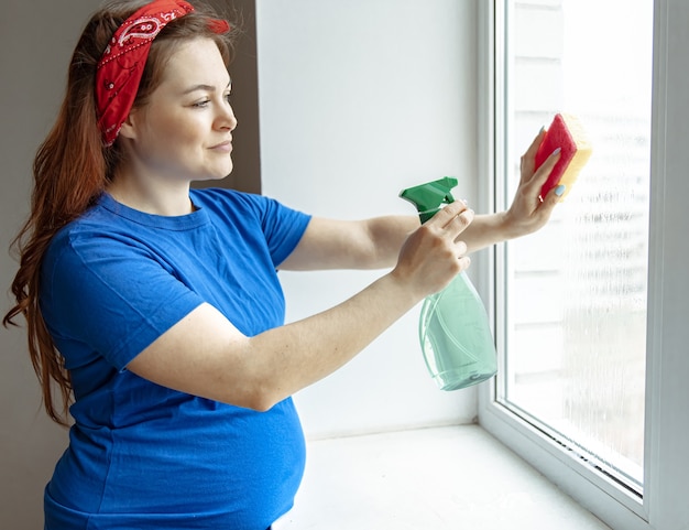 Una bella donna incinta negli ultimi mesi di gravidanza è impegnata nella pulizia e lava i vetri.