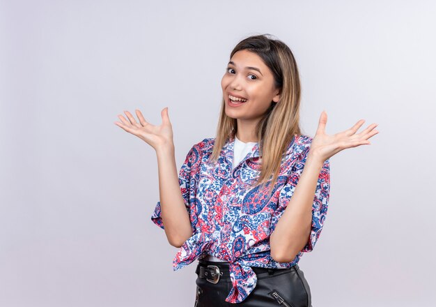 Una bella giovane donna che indossa la camicia stampata cachemire allargando le mani mentre guarda un muro bianco