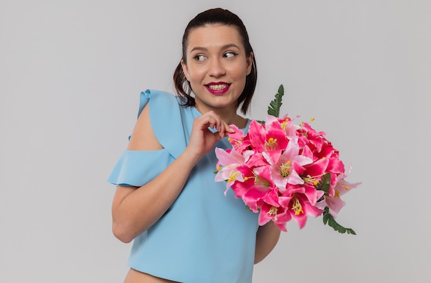 Una bella giovane donna contenta che tiene in mano un mazzo di fiori e guarda di lato