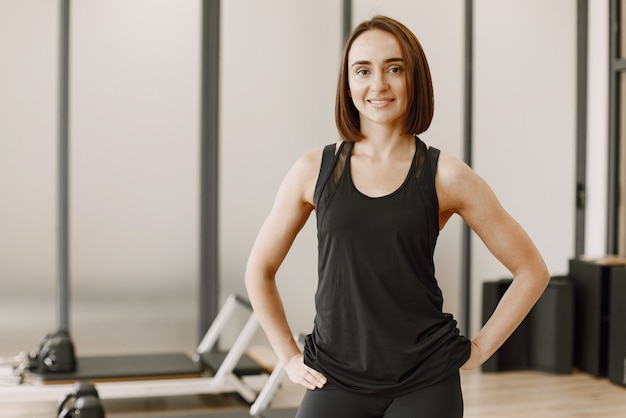 Una bella giovane donna muscolare in palestra sorride e guarda la telecamera. Donna che indossa abbigliamento sportivo nero. Concetto di concetto di potere della ragazza, sport femminile, allenamento, istruttore di fitness femminile.