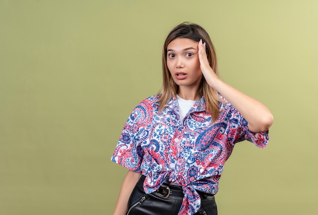 Una bella giovane donna sorprendente che porta la camicia stampata paisley che tiene la mano sulla testa