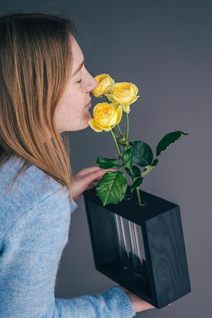 Una bella giovane donna sta annusando le rose in un vaso