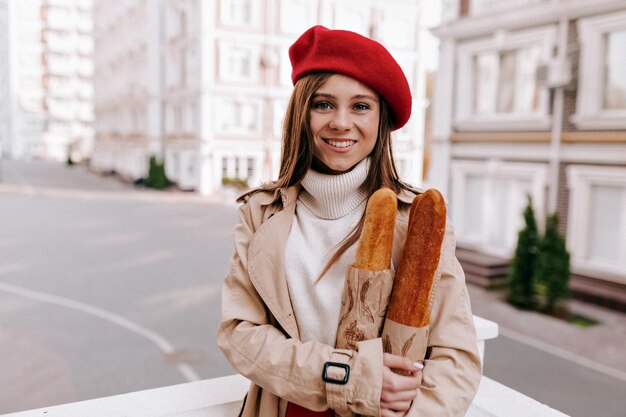 Una bella ragazza alla moda con i capelli scuri in occhiali da sole sta toccando gli occhiali e posa su sfondo beige in studio