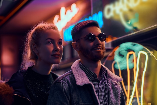 Una bella ragazza e un bell'uomo in piedi nella notte sulla strada. Insegne luminose, neon, luci.