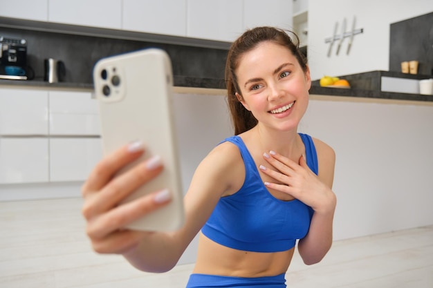 Una bella ragazza sorridente registra un video mentre fa sport a casa, guarda lo smartphone e si fa un selfie.