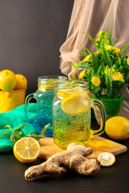 Una bevanda fresca fresca del cocktail del limone di vista frontale dentro le tazze di vetro affettate e limoni interi con i fiori sui precedenti scuri bevono la frutta del cocktail