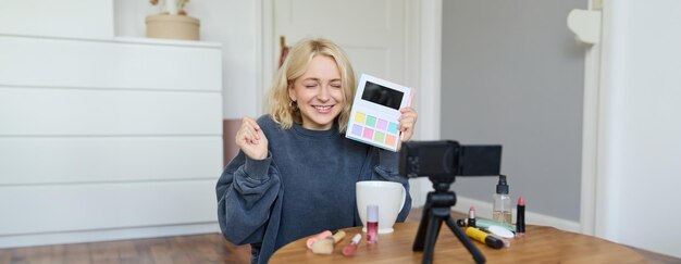 Una bionda sorridente e eccitata registra una recensione video su un nuovo blogger di stile di vita con una nuova palette di ombra agli occhi