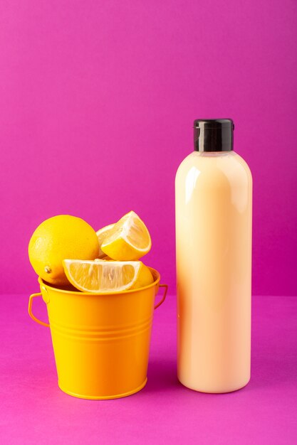 Una bottiglia di shampoo di plastica color crema vista frontale può con tappo nero con cesto pieno di limoni isolati sul viola