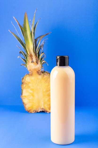 Una bottiglia di shampoo di plastica color crema vista frontale può con tappo nero isolato con ananas a fette sui capelli blu bellezza cosmetici sfondo