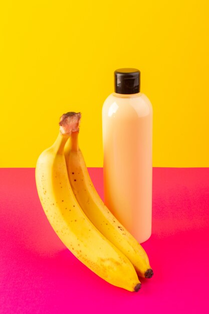 Una bottiglia di shampoo di plastica color crema vista frontale può con tappo nero isolato con banane su sfondo rosa-giallo capelli bellezza cosmetici