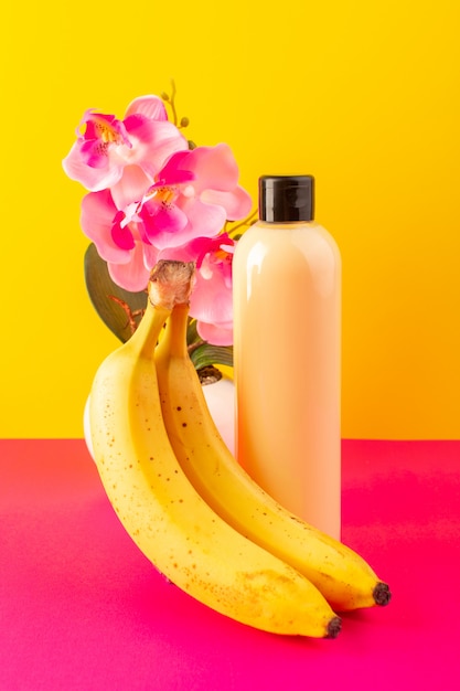 Una bottiglia di shampoo di plastica color crema vista frontale può con tappo nero isolato con banane sullo sfondo rosa-giallo capelli bellezza cosmetici