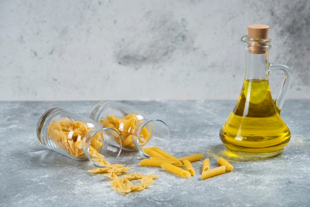 Una bottiglia di vetro di olio con maccheroni crudi.