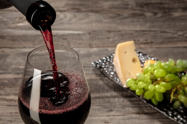 Una bottiglia e un bicchiere di vino rosso con frutta sul tavolo di legno