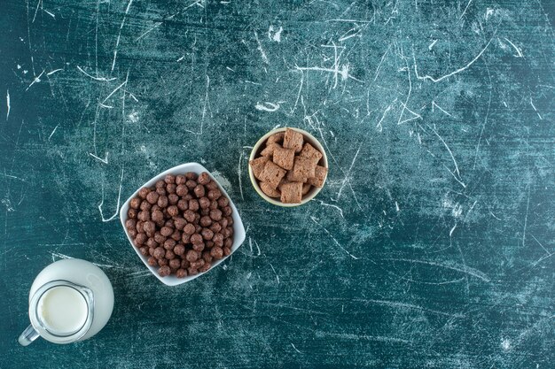 Una brocca di latte e cereali in ciotole, sul tavolo blu.