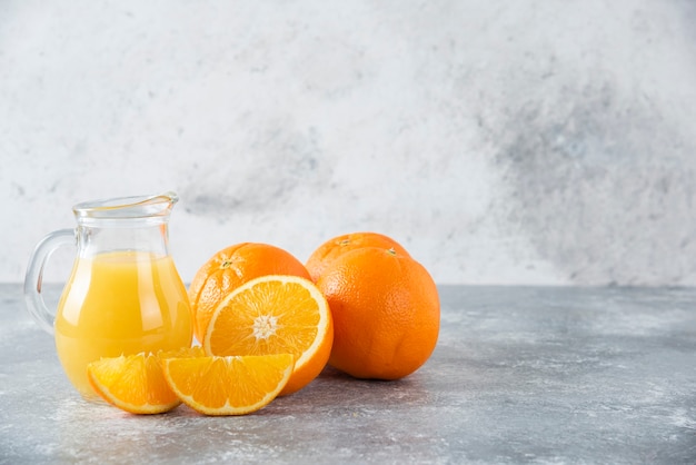 Una brocca di vetro di succo con frutta fresca di arancia sul tavolo di pietra.