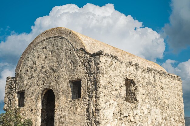 Una cappella greca abbandonata contro un cielo blu con nuvole si trova su una montagna in una città fantasma abbandonata vicino a Fethiye in Turchia Sito dell'antica città greca di Karmilissos del XVIII secolo