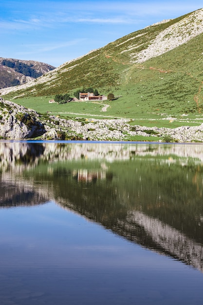 Una casa circondata da un bellissimo paesaggio e il suo riflesso sul Lago Enol in Spagna