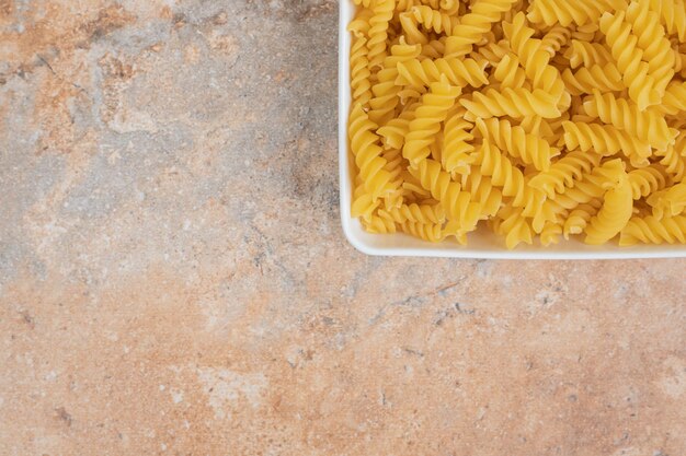 Una ciotola bianca di maccheroni non preparati sullo spazio di marmo.