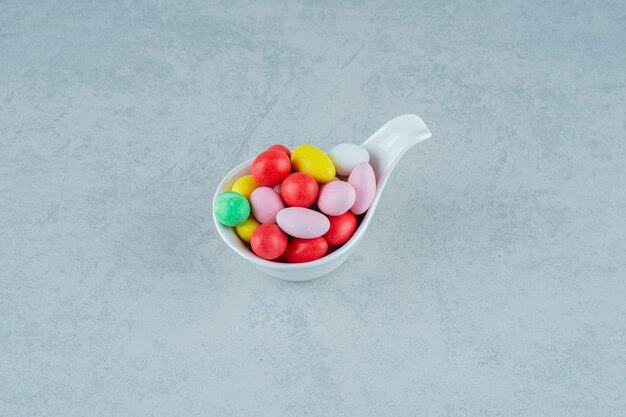 Una ciotola bianca piena di caramelle colorate dolci rotonde su una superficie bianca