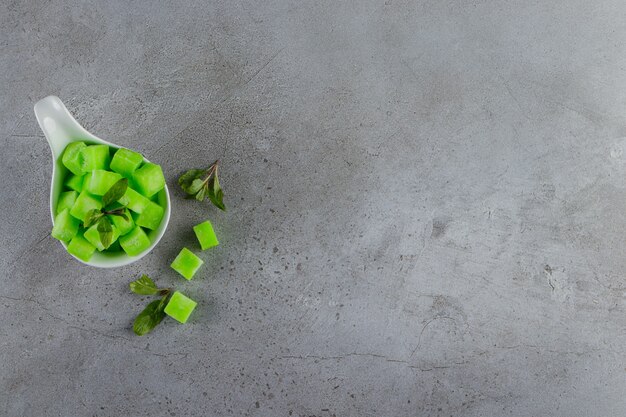 Una ciotola bianca piena di dolci caramelle verdi con foglie di menta su un tavolo di pietra.