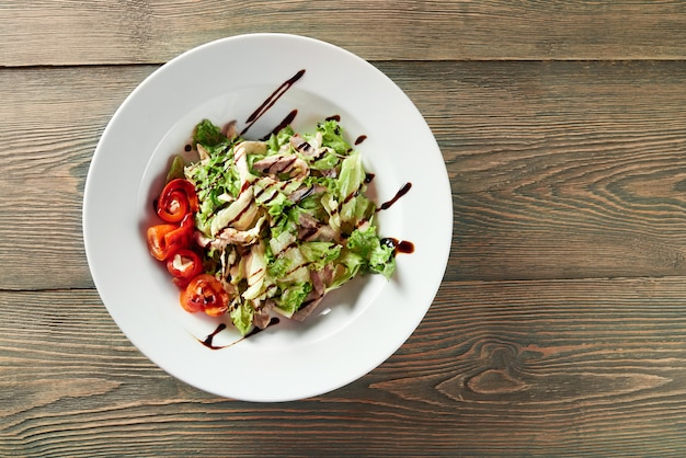 Una ciotola bianca piena di insalata di verdure con pollo alla griglia, paprika, foglie di lattuga e salsa. Sembra delizioso e gustoso.