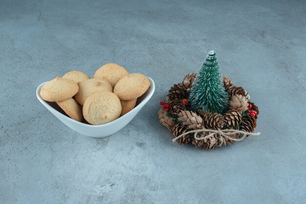 Una ciotola di biscotti accanto a una figurina di albero e una ghirlanda su una superficie di marmo