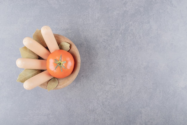 Una ciotola di legno di salsicce bollite con pomodoro rosso e foglie di alloro.