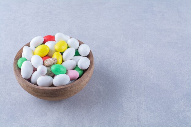 Una ciotola di legno piena di caramelle colorate di fagioli su sfondo grigio. Foto di alta qualità