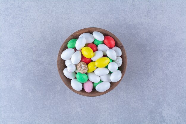 Una ciotola di legno piena di caramelle colorate di fagioli su sfondo grigio. Foto di alta qualità