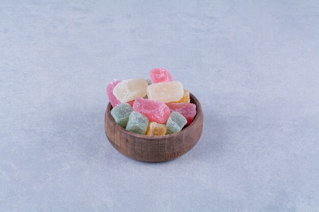 Una ciotola di legno piena di caramelle colorate di fagioli sul tavolo grigio.