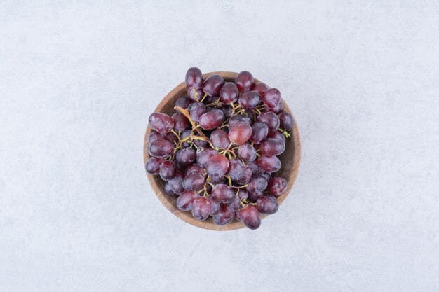 Una ciotola di legno piena di uva viola su sfondo bianco. Foto di alta qualità