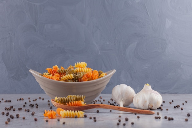 Una ciotola di pasta a spirale cruda multicolore con i grani di pepe e dell'aglio.