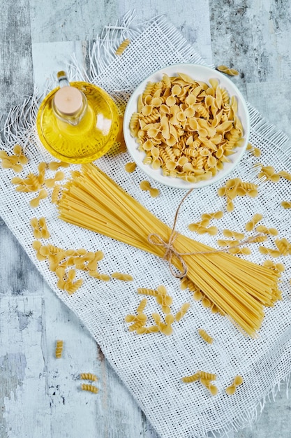 Una ciotola di pasta cruda e spaghetti con olio e tovaglia.