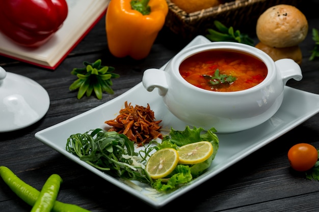 Una ciotola di zuppa di verdure in un brodo servito con insalata verde e limone