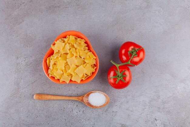 Una ciotola piena di ravioli crudi con pomodori rossi freschi e sale.