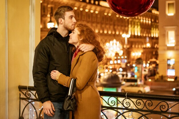 Una coppia felice sta in un abbraccio per strada la sera sotto le luci festive