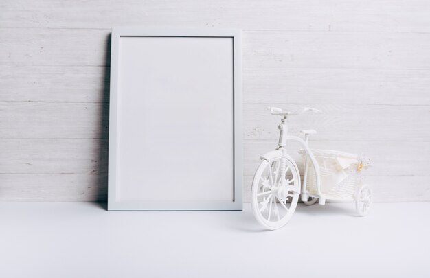 Una cornice bianca vuota vicino alla bicicletta sullo scrittorio bianco contro la parete di legno