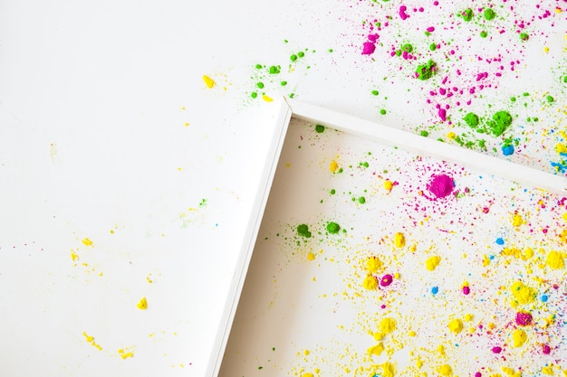 Una cornice di legno vuota su sfondi bianchi con polvere di colore holi