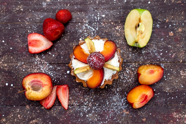 Una deliziosa piccola torta vista dall'alto con crema e frutta fresca a fette sullo scrittorio marrone torta di frutta biscotto zucchero tè