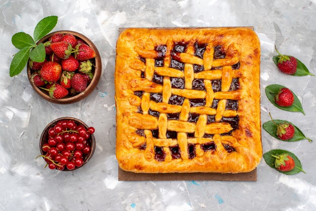 Una deliziosa torta di fragole con vista dall'alto con gelatina di fragole all'interno insieme a fragole fresche e mirtilli rossi sulla torta da scrivania grigia